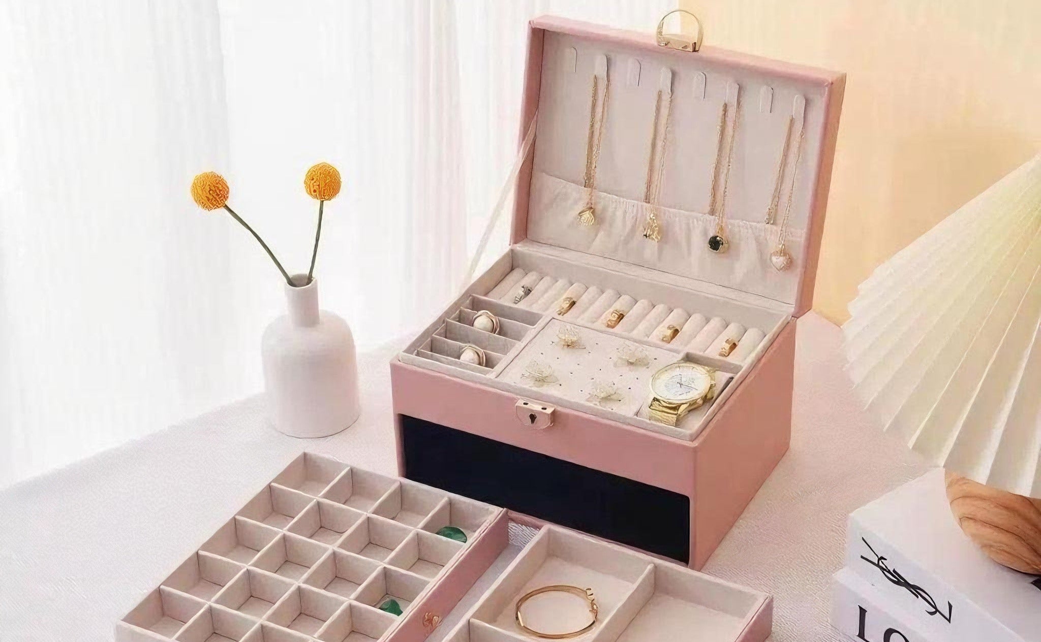Pink jewelry box with compartments filled with jewelry on a light surface.